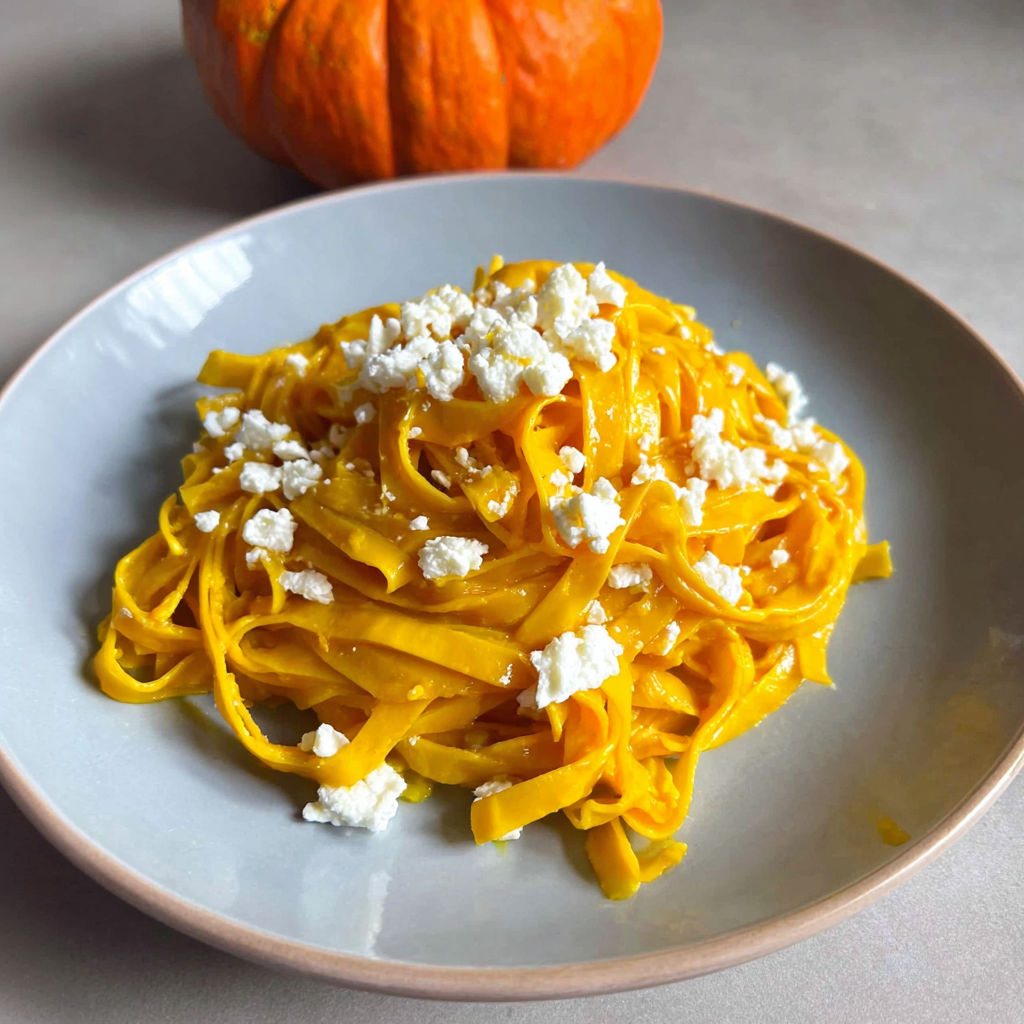 A plate of pasta with cheese and a pumpkin.