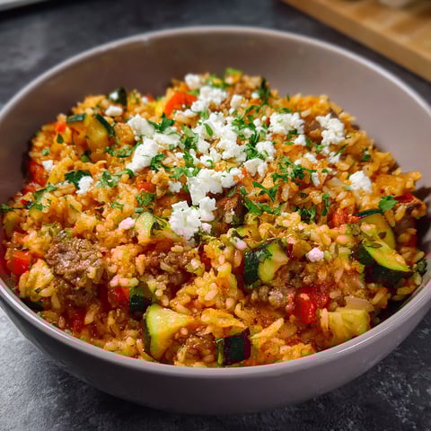 A bowl of rice with zucchini and feta cheese.