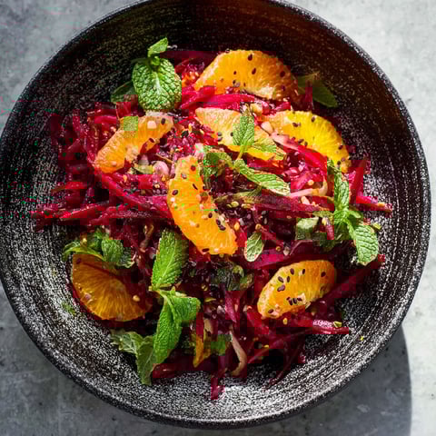 A bowl of red beets with orange slices and mint.