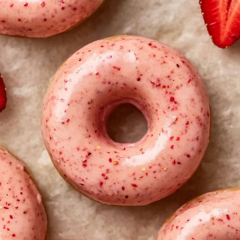 A pink glazed donut with strawberries on top.